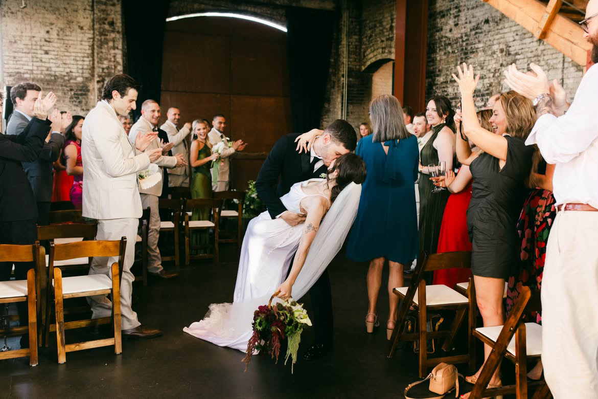 Wedding couple kissing in the aisle as guests celebrate